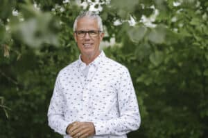 Image of Bob McCann of the MRAA dressed in white button-up dress shirt in front of greenery in Minnesota