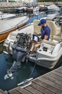 Boat tech in blue cap and polo shirt sitting on a boat using the new  TXT MULTIHUB on an outboard motor.