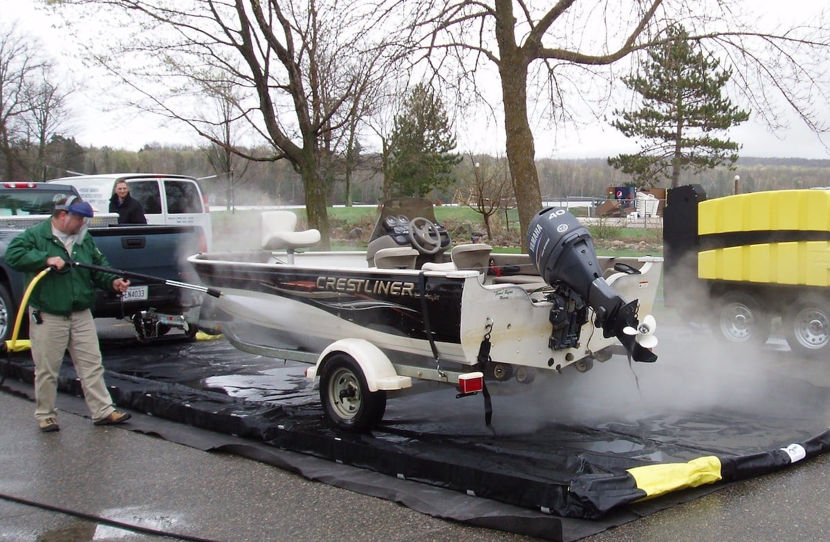 Image of fishing boat being cleaned by an official with power washer to stop the spread of invasive species. 