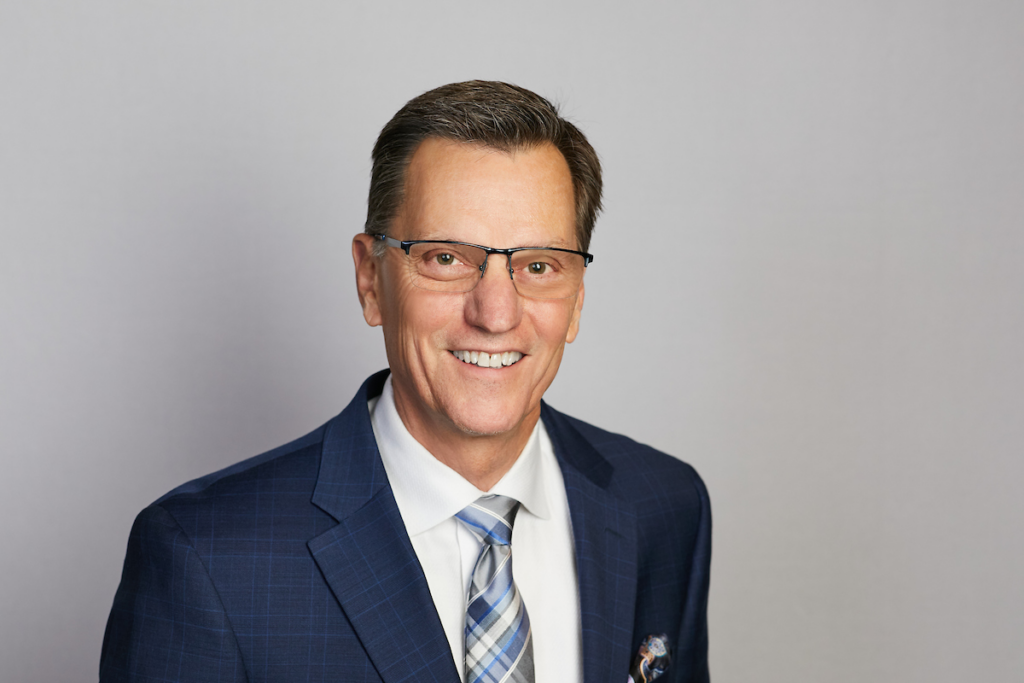 Headshot of finance expert Paul Sheldon in blue suit with white dress shirt and multicolored tie.