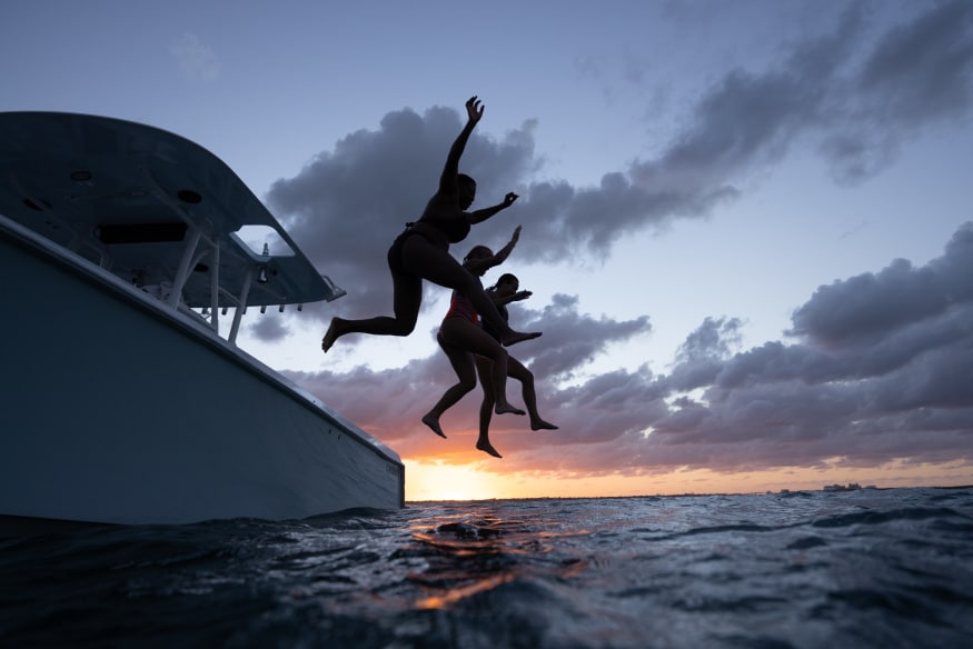 Discover Boating image of three boaters wearing PDFs jumping from anchored boat at sunset