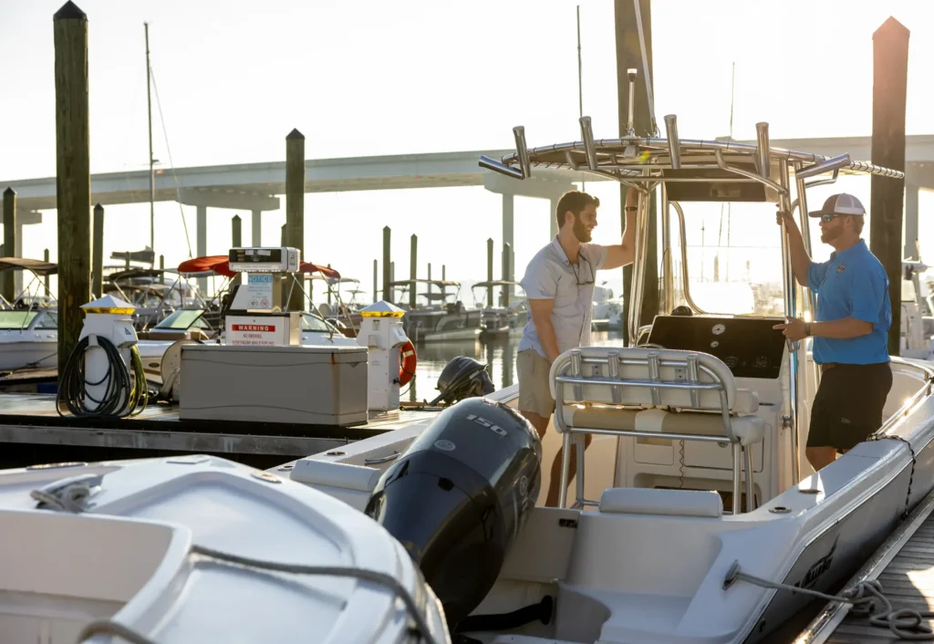 Two men standing on a certified boat dealership dock, discussing a center console boat at a marina during sunrise.